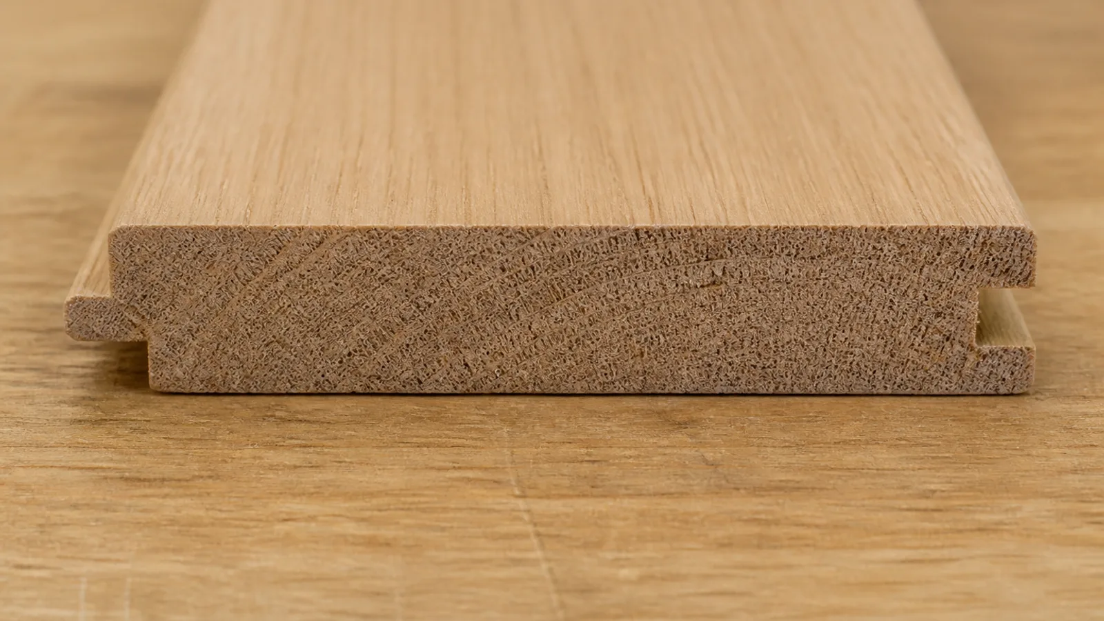 The cut end of a solid oak tongue-and-groove floorboard, showing the tongue on one side, the groove on the other and the thick band of solid wood above the tongue