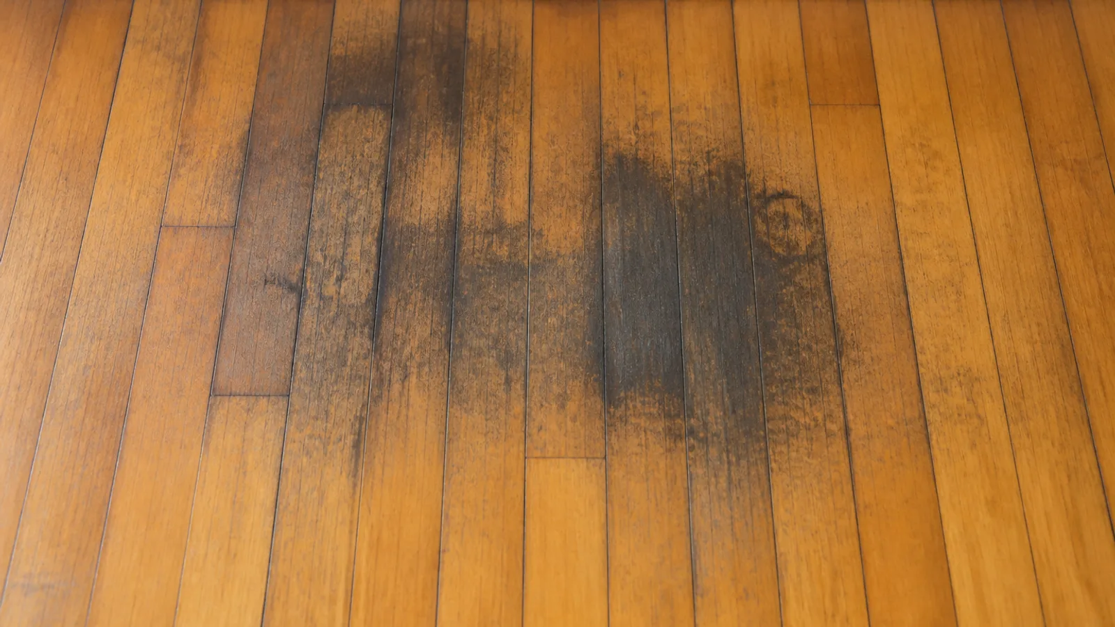 An oak strip floor with dark black-gray stains soaked into several boards, darkest along the board seams
