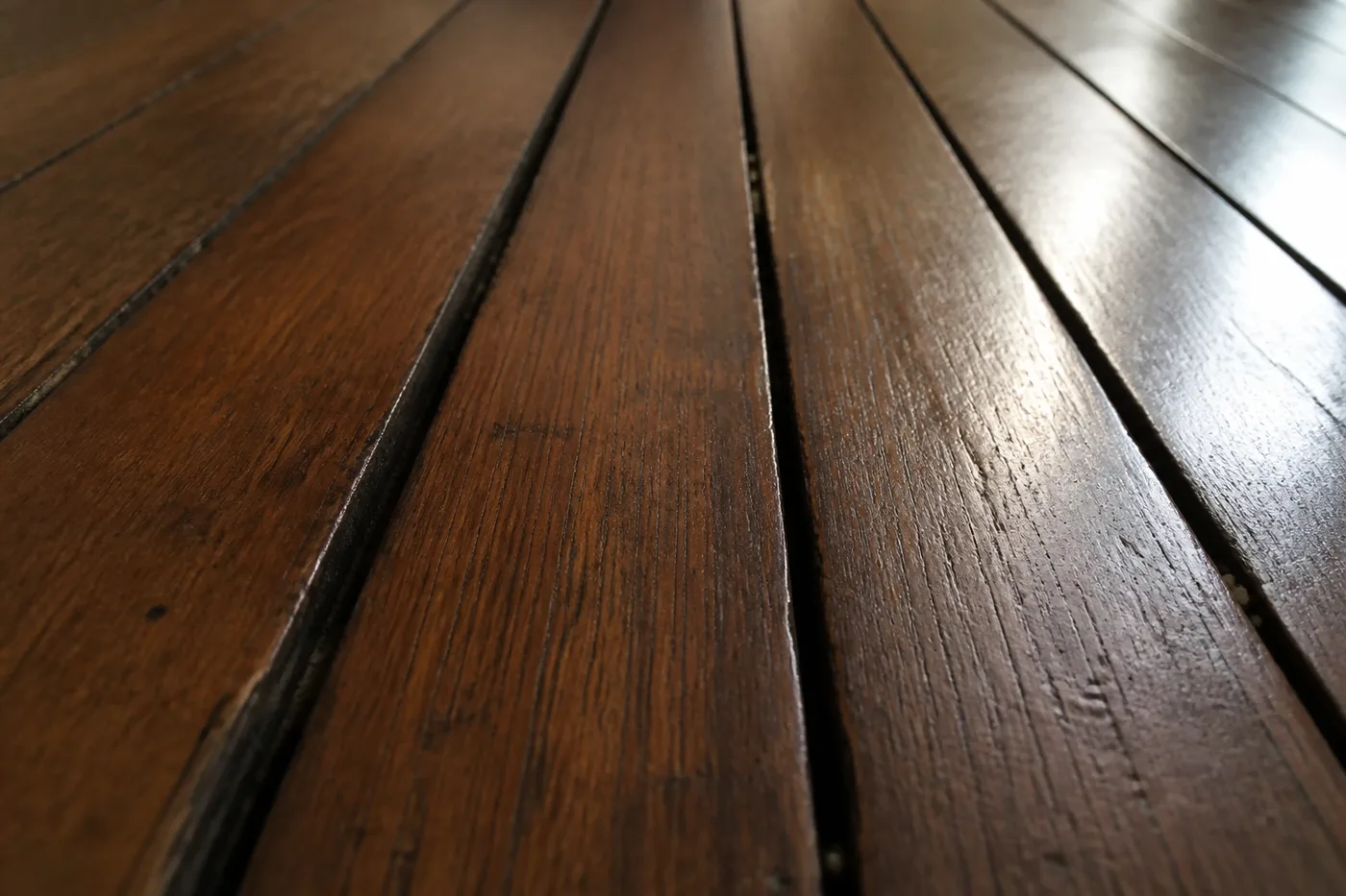 Close detail of wide dark gaps opened between old narrow oak floorboards