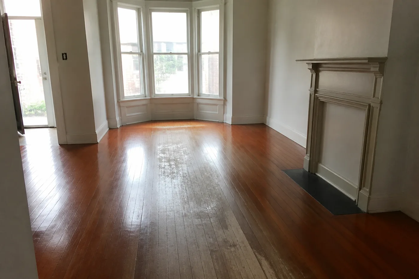A dull worn traffic path across a living room floor, finish worn through to bare wood