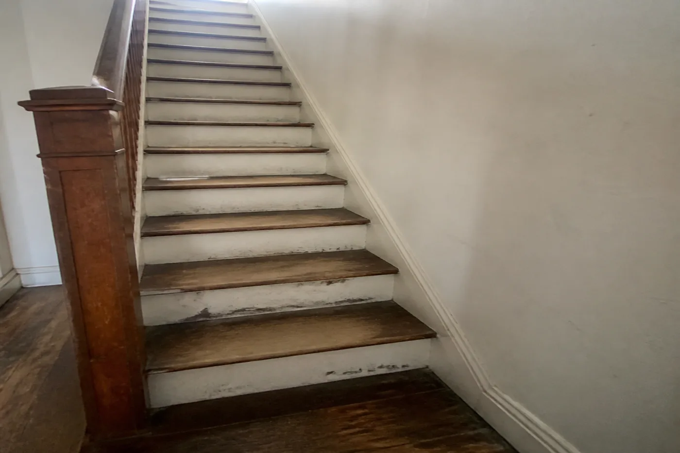 Staircase with red oak treads worn bare in the middle and chipped paint on the risers